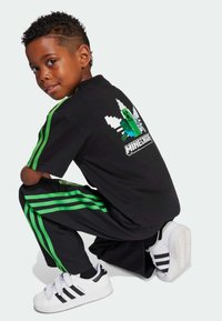Svart Minecraft-temat T-shirt med grön grafik, i kombination med svarta byxor med gröna ränder. Vita sneakers med svarta accenter.
