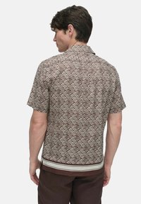 Short-sleeve brown shirt featuring a geometric diamond pattern, buttoned back design, and contrasting horizontal stripe at the hem.