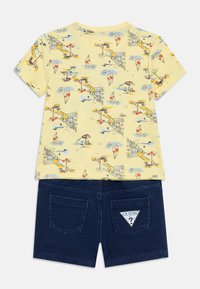 Κίτρινο κοντομάνικο T-shirt με θέμα την παραλία, συνδυασμένο με σκούρα μπλε denim σορτς που διαθέτουν τσέπες και τριγωνική ετικέτα με λογότυπο.