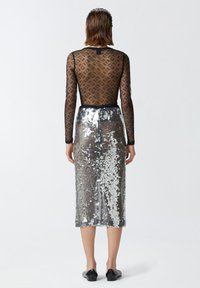 Black sheer top with patterned texture and long sleeves paired with a silver sequin midi skirt. The outfit is accessorized with black shoes.