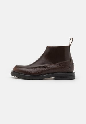Brown leather ankle boot with a textured finish, featuring a rounded toe, minimal stitching, and a low black rubber sole with a pull tab.