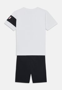 T-shirt blanc à manches courtes avec une accent noir sur la manche gauche, associé à un short noir. Les deux sont en tissu lisse, conçus pour le confort.