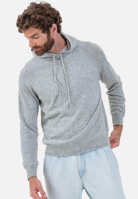 Sweat à capuche gris avec cordon de serrage, en tissu doux, doté d'une coupe décontractée et de poignets côtelés, associé à un pantalon en denim clair.
