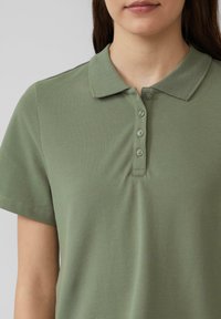 Oliwkowa koszulka polo o gładkiej fakturze, z krótkimi rękawami, zapięciem na guziki i klasycznym kołnierzykiem.