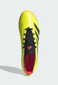 Botín de fútbol amarillo brillante con una parte superior texturizada, cordones negros y tres rayas negras. Acentos rojos en la plantilla y el collar.