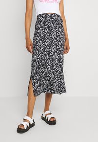 Mujer que lleva una falda midi negra con estampado floral blanco y una abertura lateral, una camiseta cropped blanca y sandalias blancas con suelas negras.