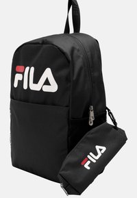 Svart ryggsäck i tyg med en framficka, dragkedjestängning och FILA-logotyp i vitt och rött. Inkluderar en avtagbar ficka.