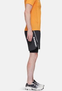 Herrträningsklädsel bestående av en orange kortärmad tröja och svarta shorts med vita detaljer. Inkluderar grå sneakers med texturerade sulor.