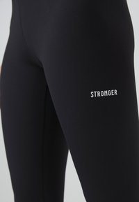 Black leggings made from stretchy, smooth material, featuring the word "STRONGER" in white text on the lower side.