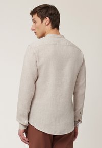 Lichtbeige linnen shirt met een relaxte pasvorm, lange mouwen, een gebogen zoom en knoopaccenten op de manchetten. Gladde textuur en subtiele weefdetails.
