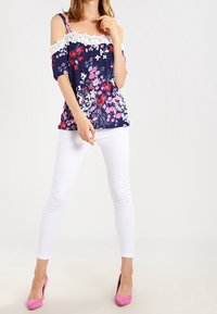 Floral navy top with white lace accents, cold shoulder design, short sleeves. Paired with white skinny jeans and pink high heels.