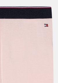 Ljust rosa tyg med midjeband i marinblått. Har en liten broderad logotyp på sidan. Slät textur och figurnära design.