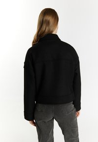 Giacca cropped nera realizzata in tessuto testurizzato con colletto e maniche. Abbinata a jeans grigio scuro a vita alta con tasche posteriori.