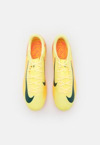 Erkli kollane jalgpallijalatsid tekstuurse pealisega, rohelise Nike s*ftiga ja oranžaga mustriga voodriga. Omab kergeid paelu ja madalat profiili.