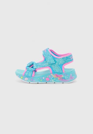 Light blue sandal with pink accents, featuring a bow, mesh straps, and a patterned sole with mermaid and sea creature designs.