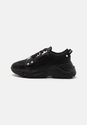 Sort chunky sneaker med mesh sider, tyk sål, snørebånd foran og hvid logo tekst på rem og hælstrop.