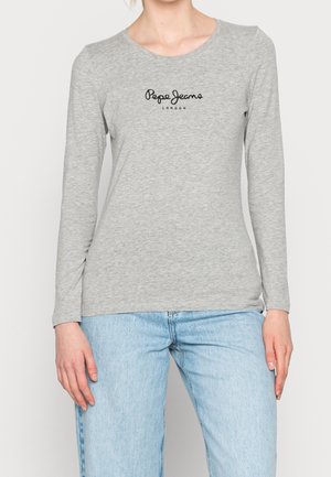 Personne portant une chemise à manches longues gris clair avec le logo "Pepe Jeans London" et un jean bleu clair, debout, bras détendus.