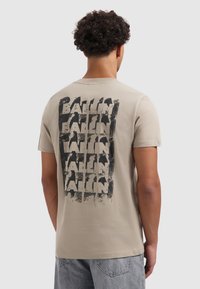 Beige katoenen t-shirt met een zwarte grafische print met de tekst "BALLIN" in herhaalde, vette letters op de achterkant. Korte mouwen, ronde hals.