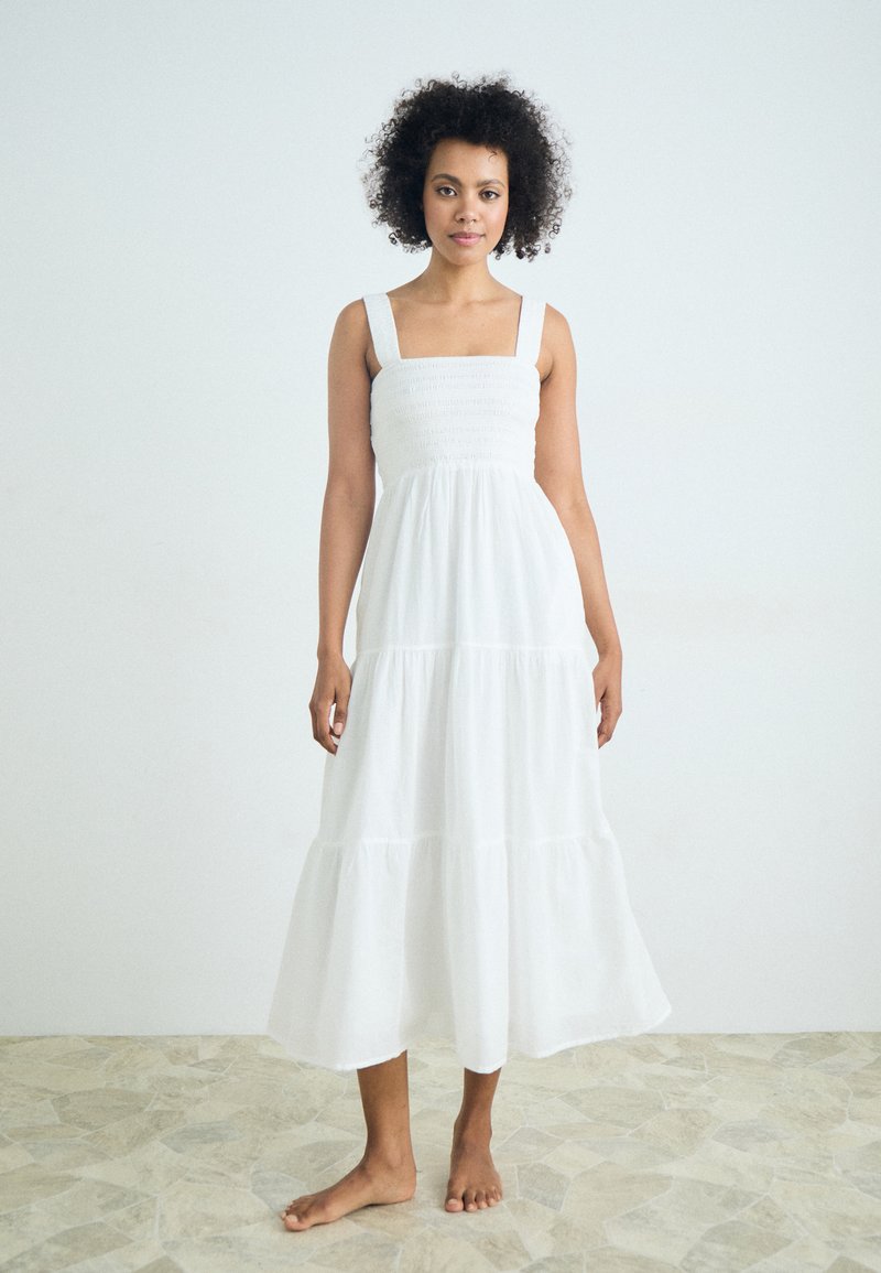 Balta, be rankovių maxi suknelė su susmulkintu liemeniu, kvadratiniu iškirpimu ir lygiais sijonais. Pagaminta iš lengvos medžiagos, turinti plazdančią siluetą.