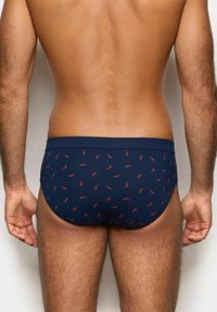 Bañadores de color azul marino con un patrón de pequeños pimientos rojos. Confeccionados en una tela elástica, presentan una cinturilla sólida y un diseño ajustado.