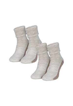 Helle beigefarbene Strumpfsocken aus Strick mit einem weichen, flauschigen Bund und einer strukturierten Oberfläche. Sie weisen einen kontrastierenden braunen Akzent an der Sohle auf, der für Grip und Stabilität sorgt.
