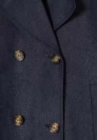 Blazer bleu foncé à double boutonnage avec col à revers et quatre boutons marron marbré disposés en deux rangées verticales.