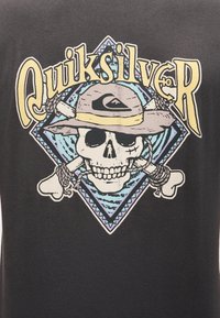 Kranium iført hat med Quiksilver-logoen, krydsede knogler bundet med reb bagved, indrammet af et blå og lilla diamantmønster.