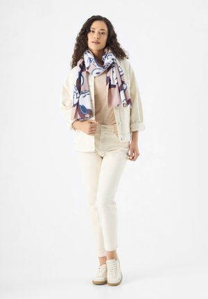 Veste blanche surdimensionnée, pull beige, jean blanc et baskets claires. Écharpe à motifs colorés avec des accents bleus, roses et blancs.