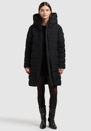 Melnā pūkains jaka ar kapuci, kas aprīkota ar rāvējslēdzēju un pogu aizdari, vertikālām virsmas gumijām, sānu kabatām un gludu, spīdīgu tekstūru.