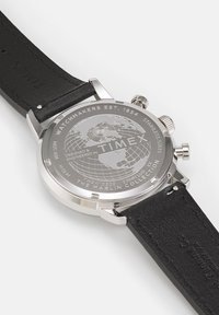 Stainless steel watch back with engraved globe design, black leather strap, features stainless steel accents and maker details.