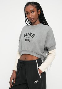 Siv sweatshirt s kratkimi rokavi z napisom "NIKE 1972" v črni barvi; v kombinaciji s črnimi športnimi hlačami z belim stranskim pasom in majhnim logotipom.