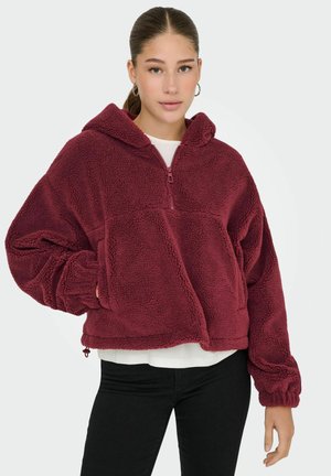 Haut en polaire bourgogne avec un zip central à moitié, poche kangourou et poignets élastiques. Tissu doux et texturé avec une coupe décontractée.