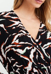 Black fabric with a wavy abstract pattern in white, brown, and green. Features a V-neck and smocked waist detail.