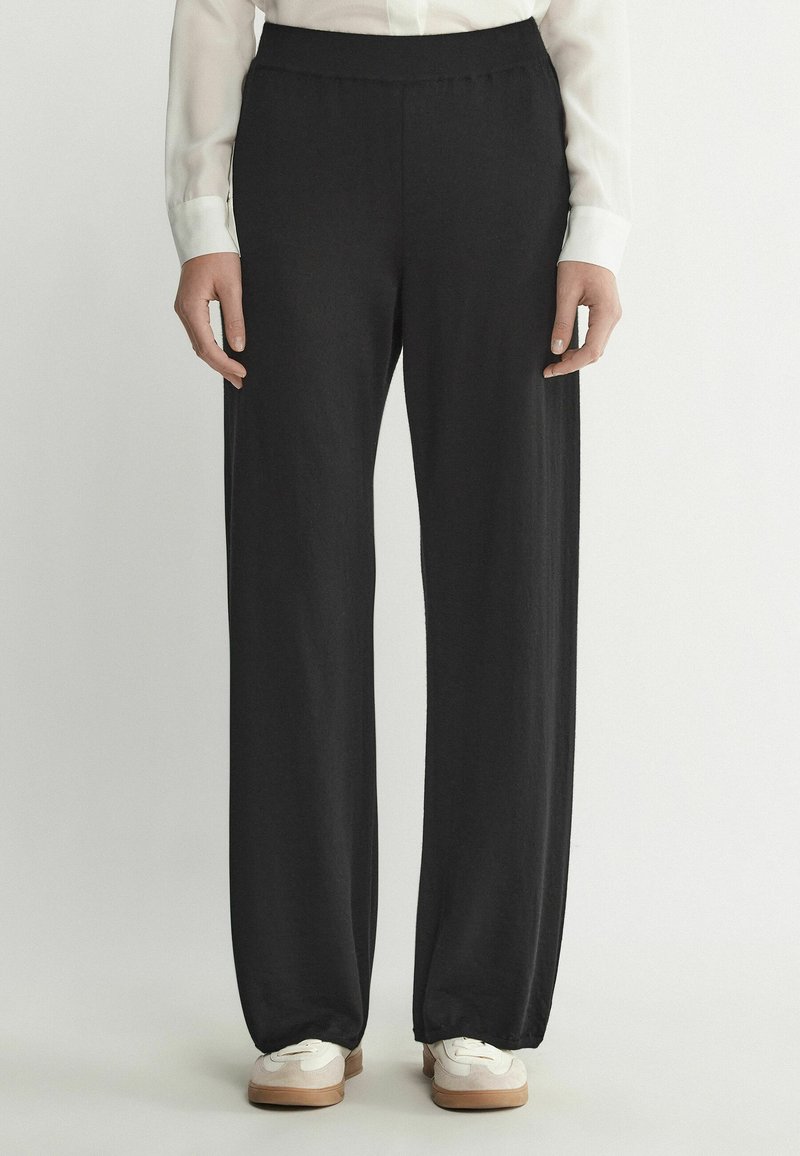 Svart vida byxor gjorda av mjukt tyg med en slät yta, med resårmidja. Matchas med vita sneakers.