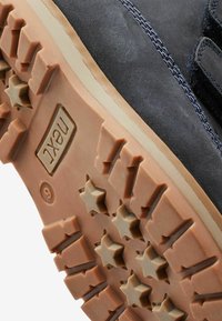 Sneakersåle med robust brunt gummi med stjernemønstre, sort struktureret overmateriale med blå syninger og logodetalje.