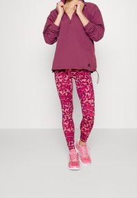 Suéter burdeos con cuello de cremallera, combinado con leggins de estampado de leopardo rosa vibrante y zapatillas deportivas rosas.