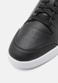 Baskets en cuir noir à finition lisse, avec des perforations sur l'avant, des lacets noirs et une semelle en caoutchouc blanche.