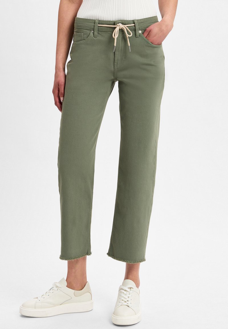 Pantaloni verde oliva a 3/4 con una vestibilità morbida, orlo sfilacciato e vita con cordoncino in beige. Abbinati a sneakers bianche.