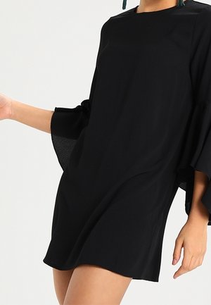 Czarna sukienka o luźnym kroju, szerokie rękawy w kształcie dzwonu i okrągły dekolt. Wykonana z lekkiego materiału o gładkiej fakturze.