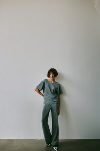 Szürke textúrájú, két részből álló szett, laza, rövid ujjú felsővel és bő szárú nadrággal, sima fehér fal előtt.