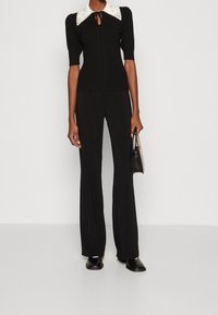 Haut noir côtelé avec col arrondi blanc, associé à un pantalon noir évasé. Le haut présente un lien de cou en forme de goutte et une texture subtile.