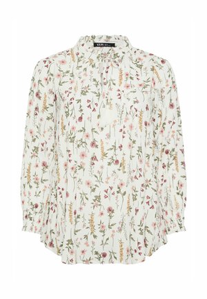 Witte blouse met lange pofmouwen, bloemenprint in roze, groen en geel, en een kleine strik bij de kraag met kwastjes.