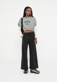 Siv sweater kratke dolžine s potiskom "NIKE 1972", v kombinaciji z črnimi širokimi trenirkami. Črne športne čevlje z sijajnimi poudarki.
