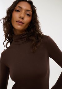 Maglia a collo alto marrone realizzata in tessuto liscio ed elastico con maniche lunghe. Il design si adatta strettamente al corpo, mettendo in risalto il suo profilo.