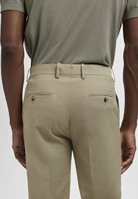 Ljusbeige skräddarsydda byxor med en slät yta, två bakfickor med rundade knappar och en slim fit-design.