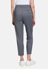 Marineblauwe broek met een getailleerde pasvorm, cropped lengte en twee achterzakken, gecombineerd met witte sneakers. Gladde stofstructuur.