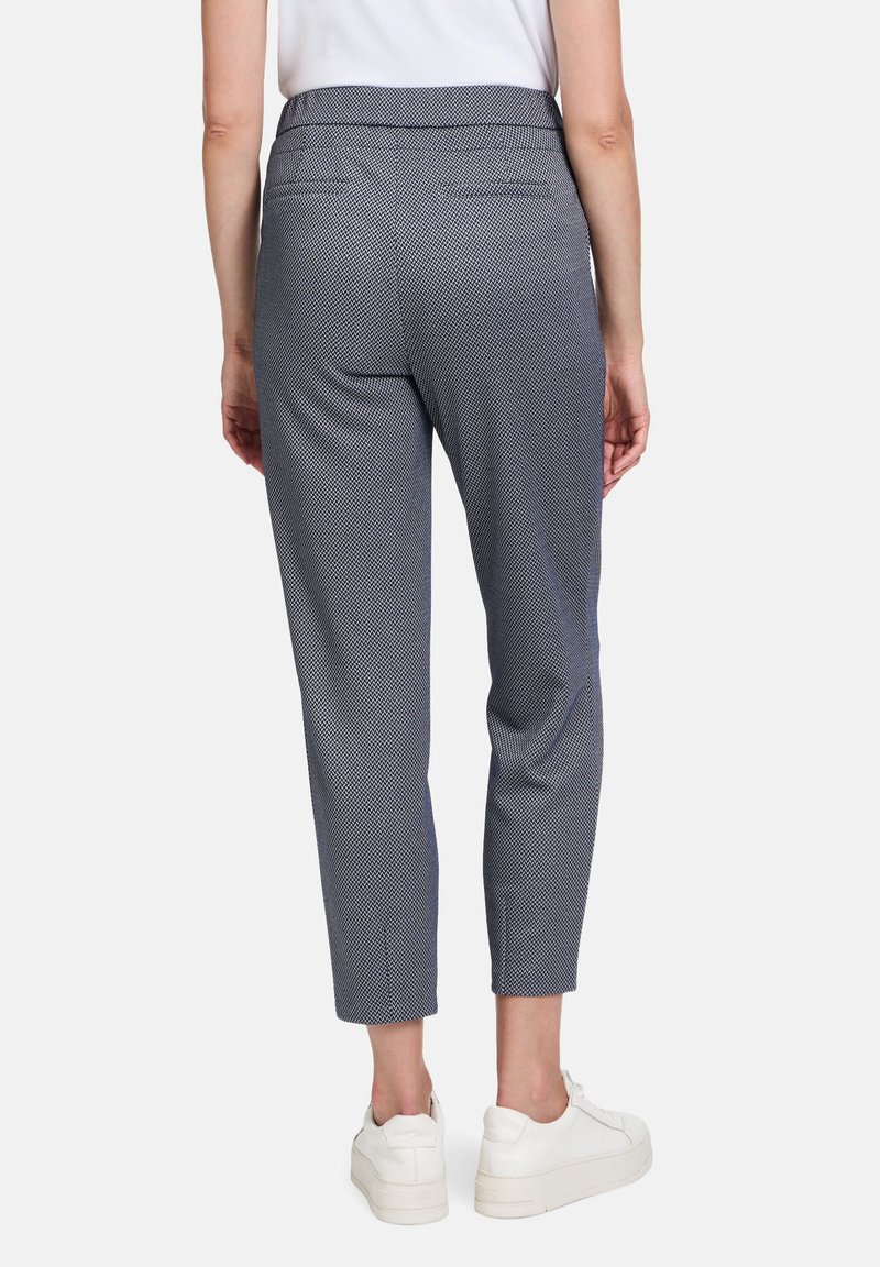 Marineblauwe broek met een getailleerde pasvorm, cropped lengte en twee achterzakken, gecombineerd met witte sneakers. Gladde stofstructuur.