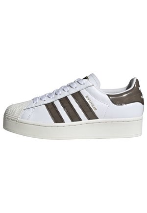Baskets Adidas Superstar blanches avec des rayures noires, embout coquillage et semelle épaisse, vue de côté montrant le texte "Superstar" sur la tige.