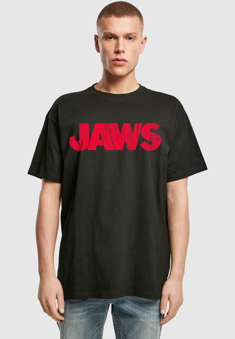 Čierne bavlnené tričko s veľkým, opotrebovaným červeným grafickým dizajnom "JAWS" na hrudi. Uvoľnený strih s krátkymi rukávmi a okrúhlym výstrihom.