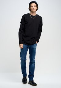 Camiseta negra superpuesta a una camisa de manga larga, jeans de denim azul y botas de cuero negro. Los accesorios incluyen un collar de cadena de metal y una boina.